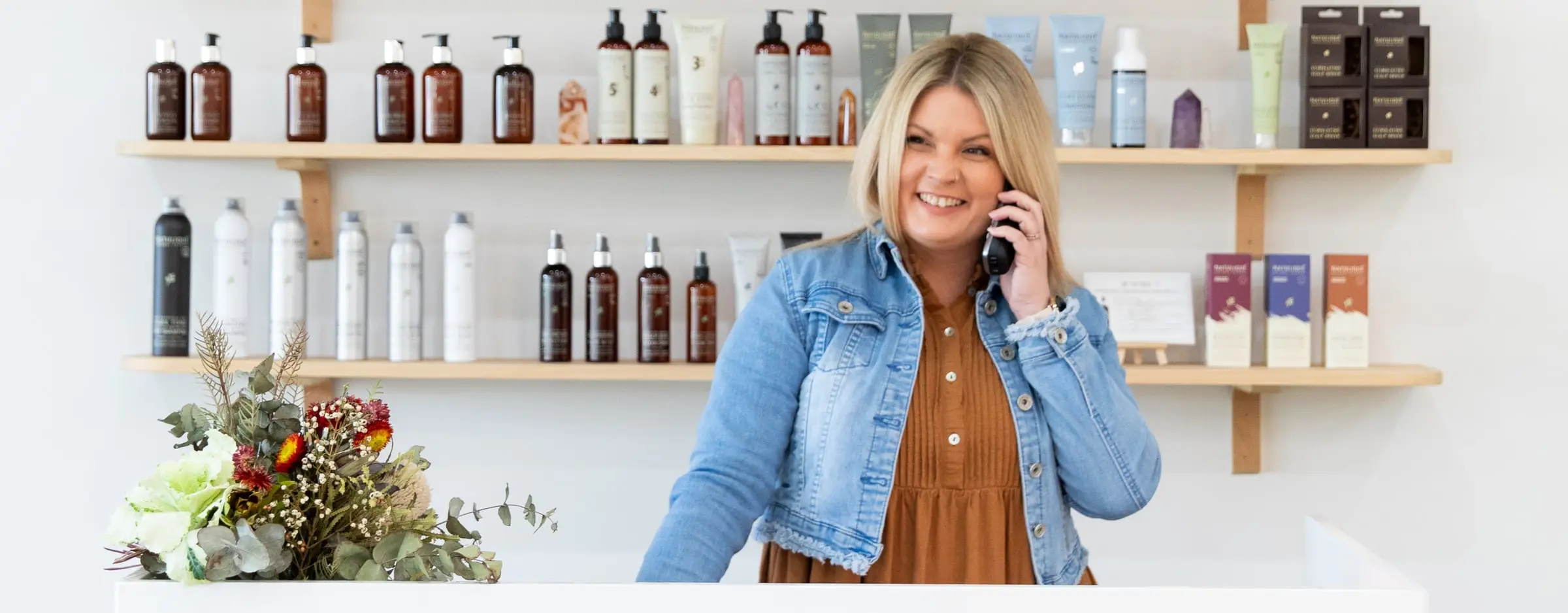Ergo and Mane hairstylist taking a booking call beside NATULIQUE organic hair products in Bridgewater